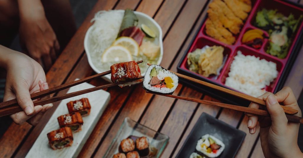 Close-up of hands holding sushi with chopsticks, showcasing Japanese cuisine over a wooden table.