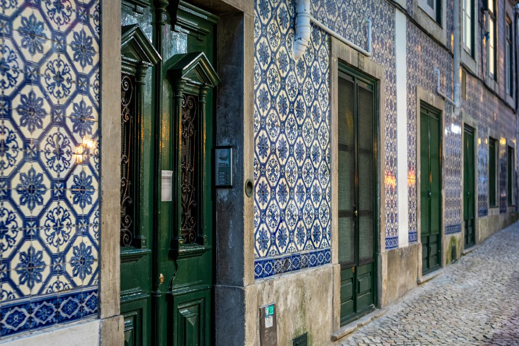 A picturesque street in Lisbon featuring iconic blue and white Portuguese tiles and green doorways.